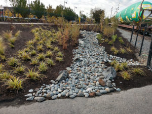 Rock-lined drainage ditch beside a train track with plants.